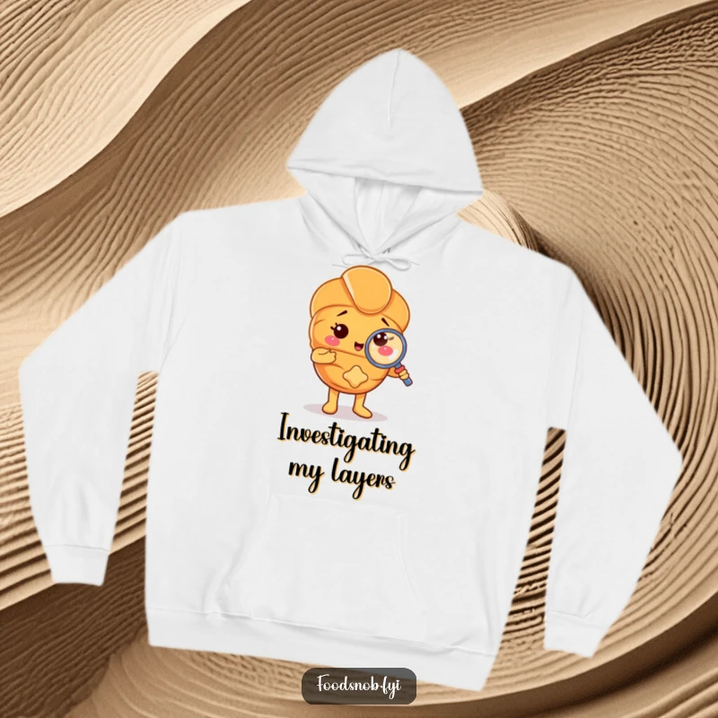 Funny hoodie with a proud croissant character using a tiny magnifying glass on a crumb, offering warmth and humorous detail. A unique pastry item.