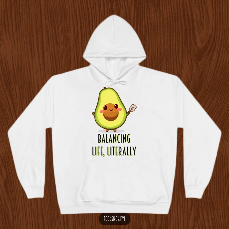 Funny hoodie with a happy avocado character balancing its pit on a tiny spatula, embodying kitchen fun and charm.